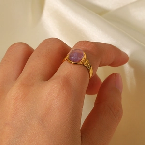 Close-up of a gold ring with a round purple gemstone on beige silk fabric