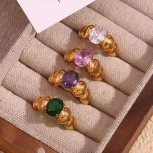 Detail of 18K gold-plated beaded rings with colorful oval gems in a beige jewelry box