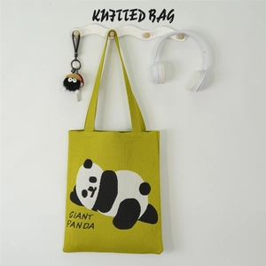 Green knitted panda tote bag hanging with white headphones and plush charm detail