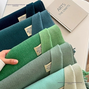 Detail view of double-sided faux cashmere scarves in green tones with fringe edge and tag