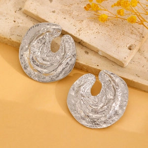 Detailed view of silver irregular textured metal stud earrings on a stone background