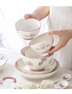 Detailed view of hand holding a white ceramic bowl with pink floral underglaze patterns