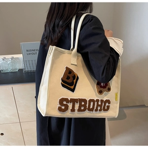 Detail of beige canvas tote bag with college style bear patch and yellow side label
