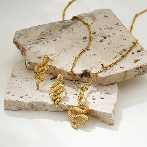 Detail of gold snake jewelry set with textured scales on beige travertine stone