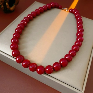Close-up of red round beaded necklace with gold clasp on beige leather jewelry box