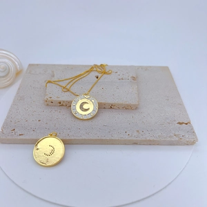 Detail of gold-plated pendant with crescent moon zircon inlay on beige stone texture