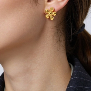Boucle d'oreille fleur minimaliste en acier inoxydable doré sur l'oreille du mannequin