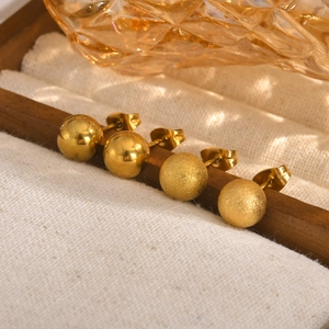 Detailed view of four golden ball earrings with polished and frosted finishes on linen