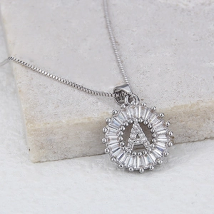 Detailed view of silver letter A pendant with cubic zirconia on beige stone