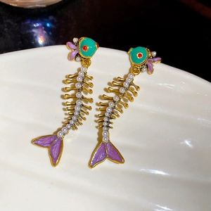 Macro shot of unique fishbone earrings with green enamel, purple fins, and white pearls