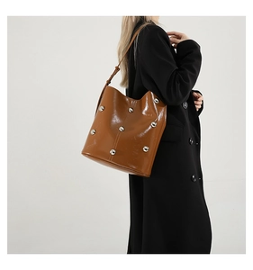 Detail view of brown bucket bag with silver rivets and adjustable strap on a model