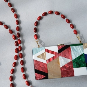 Macro view of geometric acrylic clutch with marble texture and red beaded chain