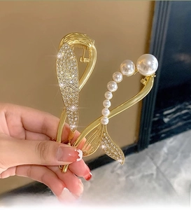 Detail of golden fishtail hair claw clip with gradient pearls and sparkling rhinestones