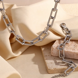 Macro shot of silver paperclip link chain with lobster clasp on beige silk and stone