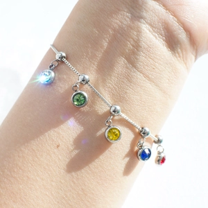 Macro shot of silver stainless steel bracelet with five vibrant birthstone pendants on wrist