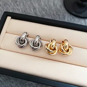 Polierte Silberne und Goldene gedrehte Metallohrstecker auf einem beigen Leder-Tablett