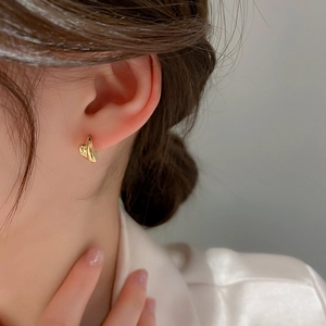 Minimalist gold heart-shaped hoop earrings with a textured geometric twist on female model