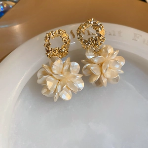 Gold plated floral stud earrings with translucent cream petals on a white plate
