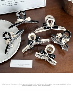 Close-up of elegant bow-shaped acetate hair claw clips in cream and black on a wooden desk