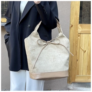 Detail of beige faux suede tote bag with decorative bow and smooth leather base splice
