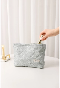 Detail of green floral jacquard makeup bag showing embossed texture and fabric label