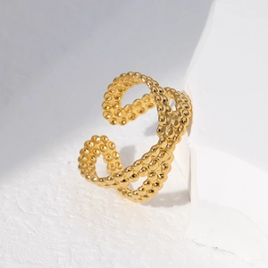 Close-up of golden beaded adjustable open ring resting on white textured stone stand