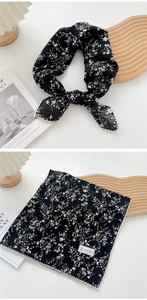 Detail of floral black square scarf with delicate white lace trim on a minimalist display