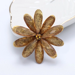 Detailed view of a gold flower brooch with amber resin petals and orange rhinestone