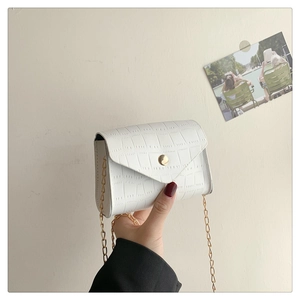 Chic white croc-embossed crossbody bag with gold chain strap held against a beige wall
