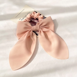 Detailaufnahme eines rosa Satin-Haargummis mit großer Schleife auf weißem Stoff