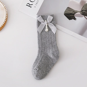 Detail of grey knitted socks featuring a satin bow and pearl pendant on a white background
