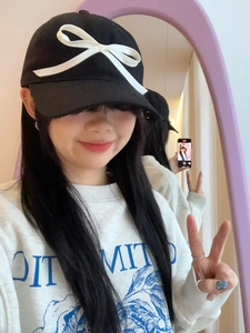 Mirror selfie showing a black baseball cap with white bow accent and a white sweatshirt