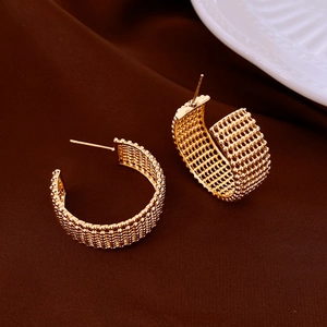 Detailed view of C-shaped gold hoop earrings featuring a textured grid pattern on the metal