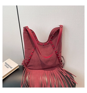 Close-up of dark red suede handbag featuring fringe tassels and sun face emblem detail