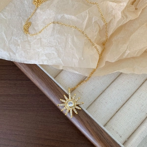 Detailed view of a gold starburst pendant necklace with zircons on a wooden jewelry box
