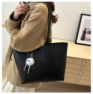 Vue latérale d'un grand sac cabas en cuir noir avec un porte-clé en peluche blanc
