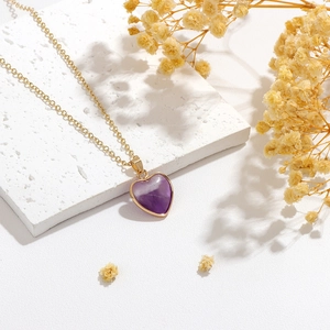 Macro shot of purple heart-shaped crystal pendant on a gold chain with dry flower decor