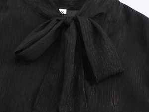 Détail du col d'une robe en mousseline noire avec nœud papillon et texture rayée