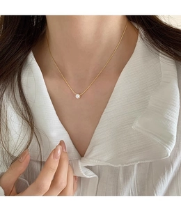 Close-up of minimalist gold zircon pendant necklace on a model wearing a white shirt