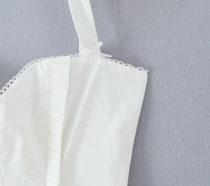 Detailed view of white halter dress featuring bow straps, lace edges, and pleated texture