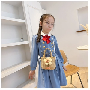 Kid modeling cute straw crossbody bag with floral and cherry decorations in a clean setting