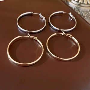 Dettaglio di orecchini a cerchio placcati oro e argento su sfondo in pelle marrone