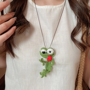 Close-up of handmade crochet frog pendant featuring green yarn and a vibrant red tongue