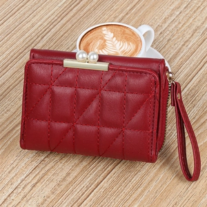 Detail of burgundy quilted wallet featuring pearl clasp and wrist strap on table
