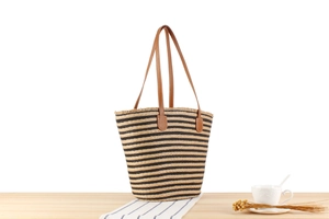 Detail of striped straw tote bag featuring brown leather handles and natural fringe trim