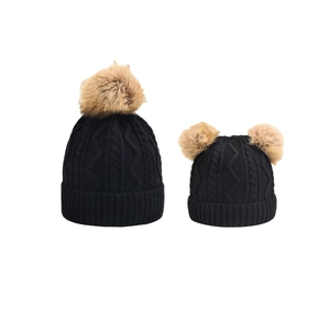 Detail view of knitted parent-child hat set in black with fluffy faux fur pom-poms
