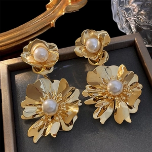 Vue détaillée d'une grande boucle d'oreille fleur dorée avec perle blanche dans son écrin