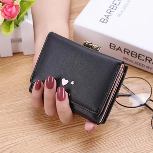 Women's black tri-fold mini wallet with gold heart clasp held by model over table