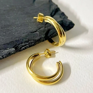 Detailed macro shot of 18k gold double-layered C-shaped earrings on stone background