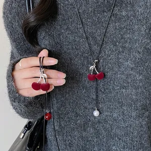Elegant flocked red cherry pendant necklace with pearls on a dark knitted sweater